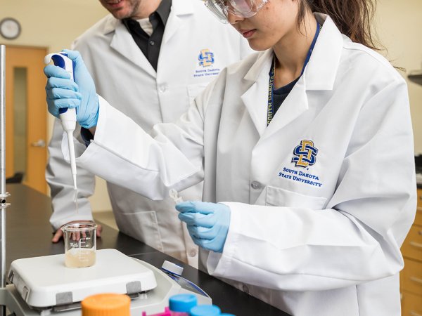 Joshua Reineke, associate professor in the Department of Pharmaceutical Sciences, assists a student working in a lab on campus.