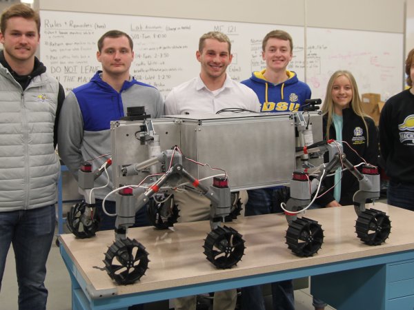 SDSU mechanical engineering students who qualified for the finals of a NASA contest are, from left, Braxton McGrath, Aiden Carstensen, graduate adviser Liam Murray, Dylan Stephens, Delaney Baumberger and Alex Schaar. They are pictured with a prototype of a rover designed to explore rugged, frozen lunar craters.