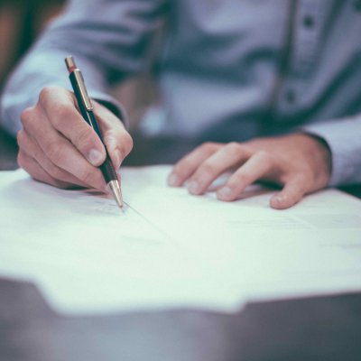 An image showing a person signing few papers scattered on a table.