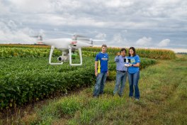 Two students and a faculty member standing by a field flying a drone.