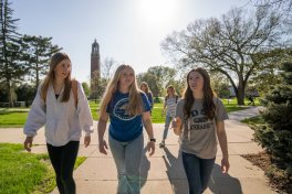 Three students walking on campus with the campanile in the background.