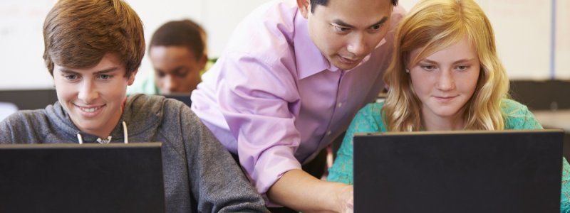 Teacher pointing at computer screen and helping a student in the classroom.