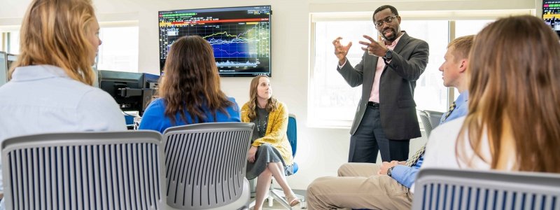 Professor speaking to a group of students in a finance lab.