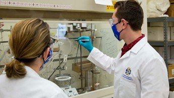 Student Timothy Paris and Dr. Willand-Charnley discussing research in front of a piece of equipment.