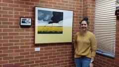 Female student in yellow sweater stands in front of brick wall 