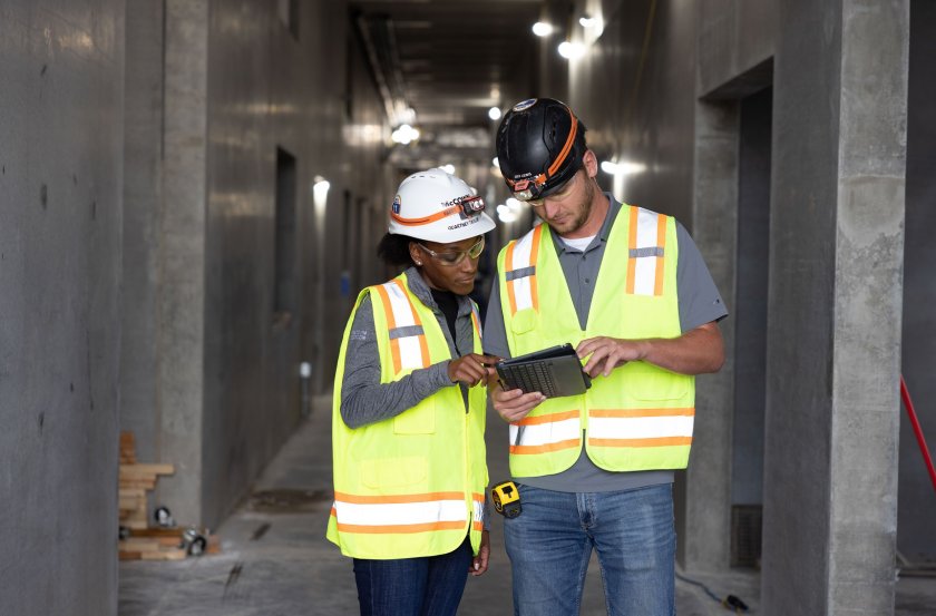 Individuals standing in construction area looking at a tablet.
