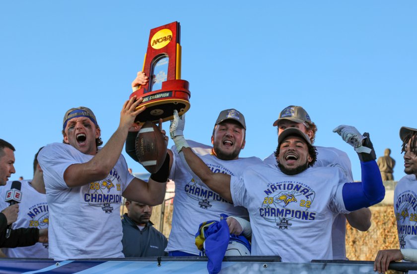 Players from the 2022 FCS Championship team yelling and holding the NCAA trophy in the air.